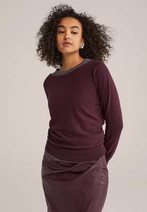Burgunderfarbener Pullover mit langen Ärmeln und kontrastierendem grauen Kragen, weicher Textur, taillierter Passform, kombiniert mit einem hochtaillierten, glänzenden burgunderfarbenen Rock.