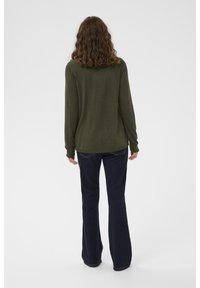 Gara piedurkņu olīvu zaļš džemperis, viegls adījums, brīvs kropls, saskaņots ar tumši ziliem zvīņotiem džinsiem, vienkāršs dizains, bez redzamiem rakstiem vai aparatūras elementiem.