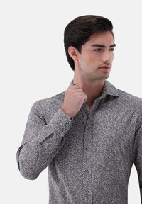 Braune Bluse mit einem kleinen Blumenmuster, Knopfverschluss und langen Ärmeln. Der Stoff hat eine glatte Textur und eine taillierte Passform.