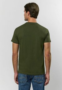 Olivově zelené tričko s krátkým rukávem vyrobené z měkké látky, s klasickým kulatým výstřihem a volným střihem, kombinované s vybledlými modrými džíny.