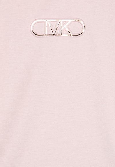 Chemise en coton rose clair avec un patch logo en relief et brillant en forme circulaire sur la poitrine, présentant une texture lisse et sans motifs supplémentaires.