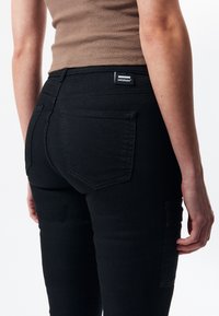 Czarne dżinsy z dopasowanym krojem, wyposażone w tylne kieszenie i metkę przy pasku. Gładka faktura i czyste linie.
