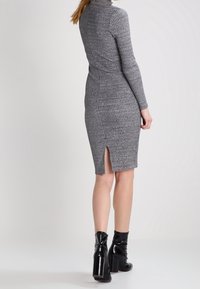 Dopasowana szara dzianinowa sukienka z długimi rękawami, wzorzystą fakturą i rozcięciem z tyłu, w połączeniu z czarnymi botkami na obcasie.
