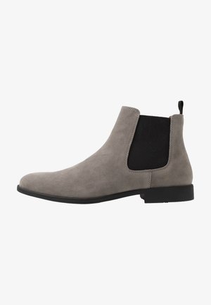 Botte Chelsea en daim gris avec panneau latéral élastique noir, semelle noire et languette de traction au talon, vue de profil sur fond blanc.