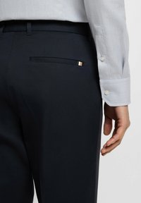 Marinblå dressbyxor med en slät textur, i slim fit. En bakficka framhävd av en guld- och svart detalj.