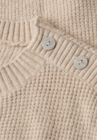 Gros plan sur un tissu de pull en tricot beige montrant un col côtelé avec deux boutons ronds de couleur claire.