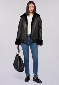 Černá kožená bunda se širokým límcem a černou umělou kožešinou, kombinovaná s modrými džíny a černou kabelem ve tvaru kýble. Boty jsou černé mokasíny.