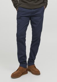 Marineblaue Chinos aus weicher Baumwolle mit einem engen Schnitt. Kombiniert mit braunen Wildlederschuhen mit gesteppten Details und flacher Sohle.