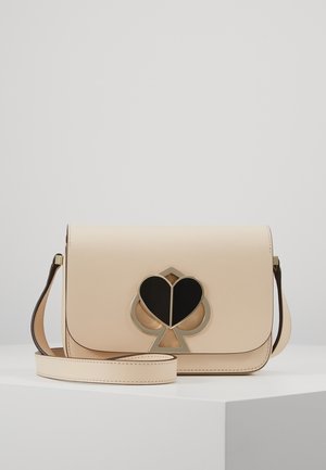 Beige leren crossbodytas met verstelbare riem en zwart-gouden hartvormig schoppenembleem op de voorflap.