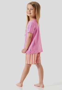 T-shirt en coton rose clair avec un graphique ludique, associé à un short rayé coloré dans des tons d'orange, de jaune et de rouge.