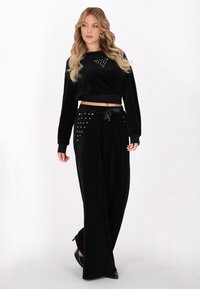 Czarny komplet dresowy z weluru, składający się z krótkiej bluzki z długim rękawem ozdobionej ćwiekami oraz szerokich spodni z bocznymi akcentami.