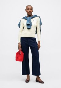 Κρεμ πουλόβερ με πλεξίδες, μπλε παντελόνι με φαρδιές γραμμές, τζιν μπουφάν ριγμένο στους ώμους, κόκκινη τσάντα και καφέ μπαλαρίνες. Απλή και καθημερινή εμφάνιση.