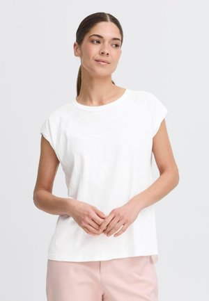 T-shirt blanc à manches courtes en tissu doux, avec une coupe décontractée, un col rond et des manches raglan, associé à un pantalon rose.