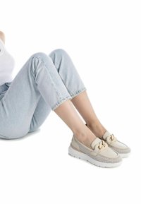 Scarpe slip-on beige con un dettaglio annodato, tomaia in rete e suola bianca. Design testurizzato con una finitura liscia. Indossate con jeans denim azzurri chiari.