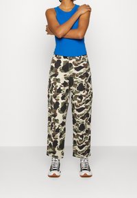 Niebieski top bez rękawów połączony z kamuflażowymi spodniami cargo. Spodnie posiadają kieszenie i mieszankę zielonych, brązowych oraz czarnych wzorów. Białe sneakersy.