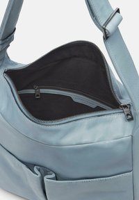Borsa in pelle blu morbida con apertura superiore che rivela un interno nero. Include una tasca con zip e tasche esterne piatte per la conservazione.