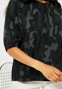 Top nero e grigio con motivo camouflage realizzato in tessuto leggero, caratterizzato da un colletto arricciato e maniche a sbuffo corte.