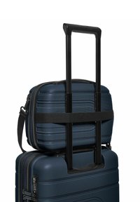 Marineblauw hard-shell kofferset met een gestructureerd oppervlak, voorzien van een telescopische handgreep en een kruisband die een kleinere koffer bovenop beveiligt.