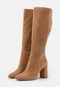 Bottes marron en daim jusqu'au genou avec un bout pointu et un talon carré. Texture lisse avec des coutures minimales et une silhouette ajustée.