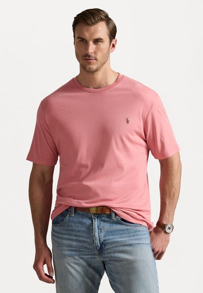 Tricou roz din bumbac, cu mâneci scurte, guler rotund și un mic logo brodat pe piept, asociat cu blugi de culoare albastru deschis.