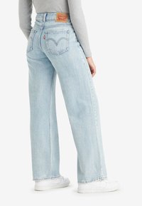 Ljusblå högmidjade jeans i denim med rak ben, subtila slitningar och en läderlogotyp på baksidan.