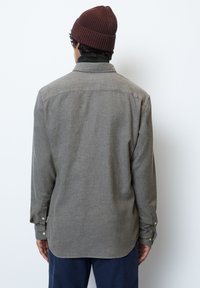 Gray wool blend shirt with long sleeves, button cuffs, and a curved hem; paired with a maroon ribbed beanie for added warmth.