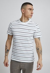 Hvit bomull t-skjorte med marineblå og lyseblå striper, har rund hals, korte ermer og liten logo på brystet.