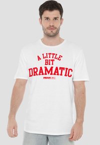 White cotton T-shirt featuring bold red lettering that reads "A LITTLE BIT DRAMATIC" with "MEAN GIRLS" logo underneath. Short sleeves, relaxed fit.