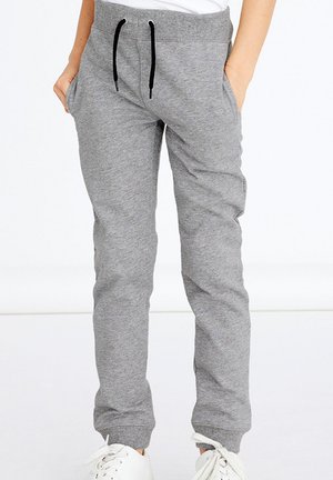 Graue Sweatpants aus Baumwollmischung mit verstellbarem schwarzen Kordelzug, seitlichen Taschen, schmal zulaufenden Beinen und gerippten Bündchen. Weiße Sneaker ergänzen das Outfit.