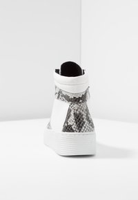 Vita högtoppssneakers med mörka ormskinnsmönstrade detaljer, strukturerad läder och en strukturerad vit gummisula. Bakre dragkedjedetalj.