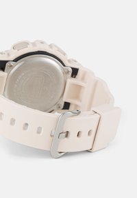 Montre avec un bracelet en silicone rose clair, dotée d'un dos en acier inoxydable, d'une boucle ajustable et d'accents texturés sur le boîtier.