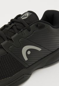 Schwarzer Sportschuh mit einem Obermaterial aus Mesh, Gummisohle und strukturierten Elementen. Beinhaltet Schnürsenkel und ein graues Logoakzent an der Seite.