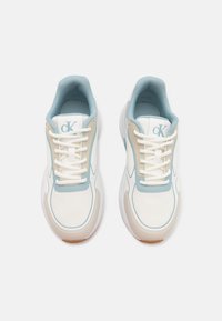 White athletic shoes with light blue accents, textured mesh upper, padded collar, contrasting sole, and logo on tongue. Laced design.