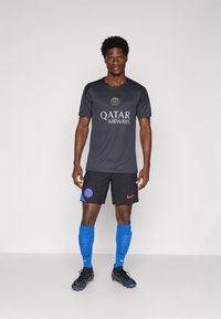 Męski strój piłkarski składający się z ciemnoszarego trykotu z logo "QATAR AIRWAYS", czarnych spodenek z niebieskimi i czerwonymi akcentami oraz niebieskich skarpet.