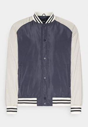 Casaco bomber azul-marinho e cinza claro com frente de botão de pressão, punhos e barra canelados listrados, e textura de tecido liso e brilhante.