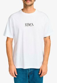 Camiseta de algodón blanca con el texto negro "RVCA" en una fuente decorativa en el pecho. Corte estándar con mangas cortas y cuello redondo.