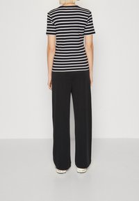 Mustat leveälahkeiset housut yhdistettynä musta-valkopalloraitaisiin lyhythihaisiin paitoihin. Paidassa on pyöreä pääntie ja pehmeä kangas.