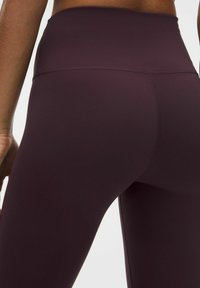 Leggings bordeaux a vita alta realizzati in un tessuto liscio e elastico, con cuciture piatte e un design aderente per comfort e supporto.