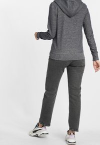 Donkere grijze hoodie met een gestructureerde afwerking en een capuchon, gecombineerd met donkergrijze broek met rechte pijpen en meerkleurige sportschoenen.