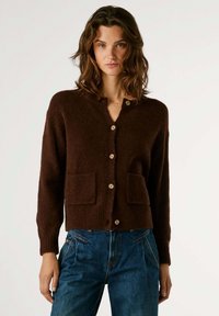 Rudas vilnos kardiganas su V formos iškirpte, dviem priekinėm kišenėm ir mygtukų užsegimu. Yra gomurėlių rankovės ir apatinė kraštinė, švelni tekstūra.