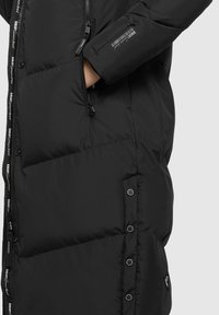 Piumino nero con design trapuntato, caratterizzato da un alto colletto, chiusure con zip e bottoni a pressione, e un branding stampato discreto sulla zip.
