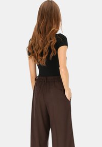 Czarny dopasowany top w połączeniu z brązowymi szerokimi spodniami z bocznymi kieszeniami i ściągaczem w pasie. Włosy rozpuszczone, falowane.