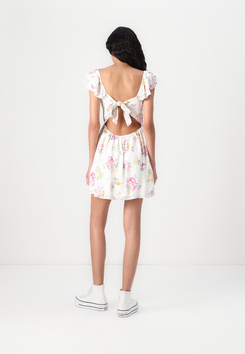 Blumenmuster-Kleid in Weiß mit Rüschensleeven, offenem Rücken und Schleifendetail. Fließender Rock, elastischer Bund, kombiniert mit weißen High-Top-Sneakern.