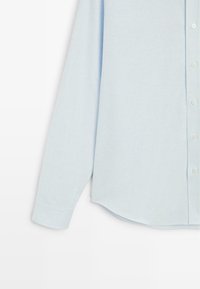 Camicia azzurro chiaro a maniche lunghe con bottoni, realizzata in tessuto a coste; presenta un orlo arrotondato e polsini standard.