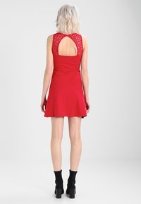 Czerwona sukienka z rozkloszowanym dołem, koronkowym tyłem i wycięciem w kształcie łezki. Gładki materiał i bez rękawów. Założona z czarnymi botkami do kostki.