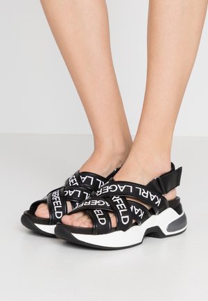 Sandales noires avec le logo blanc Karl Lagerfeld, dotées de plusieurs sangles et d'une semelle intermédiaire épaisse, rembourrée et blanche. Conception à bout ouvert.