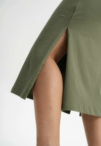 Olijfgroene rok van zacht materiaal, met een hoge zijsplit. De zoom is recht, met een nette afwerking en zonder extra accenten.