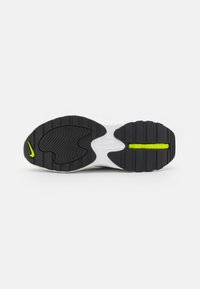 Semelle d’une basket avec une bande de roulement noire, une semelle intermédiaire blanche et des détails jaune néon, y compris un petit logo swoosh près du talon.