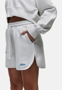 Pantaloni corti bianchi in tessuto morbido con vita elasticizzata, tasche laterali e testo blu ricamato sull'orlo. Presenta un design con spacco laterale.