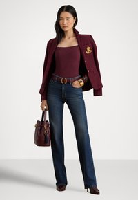 Nő bordó blézert visel vállán átdobva, hozzá illő felsőt, sötétkék farmert, barna övet, magassarkút, és bordó táskát hord.